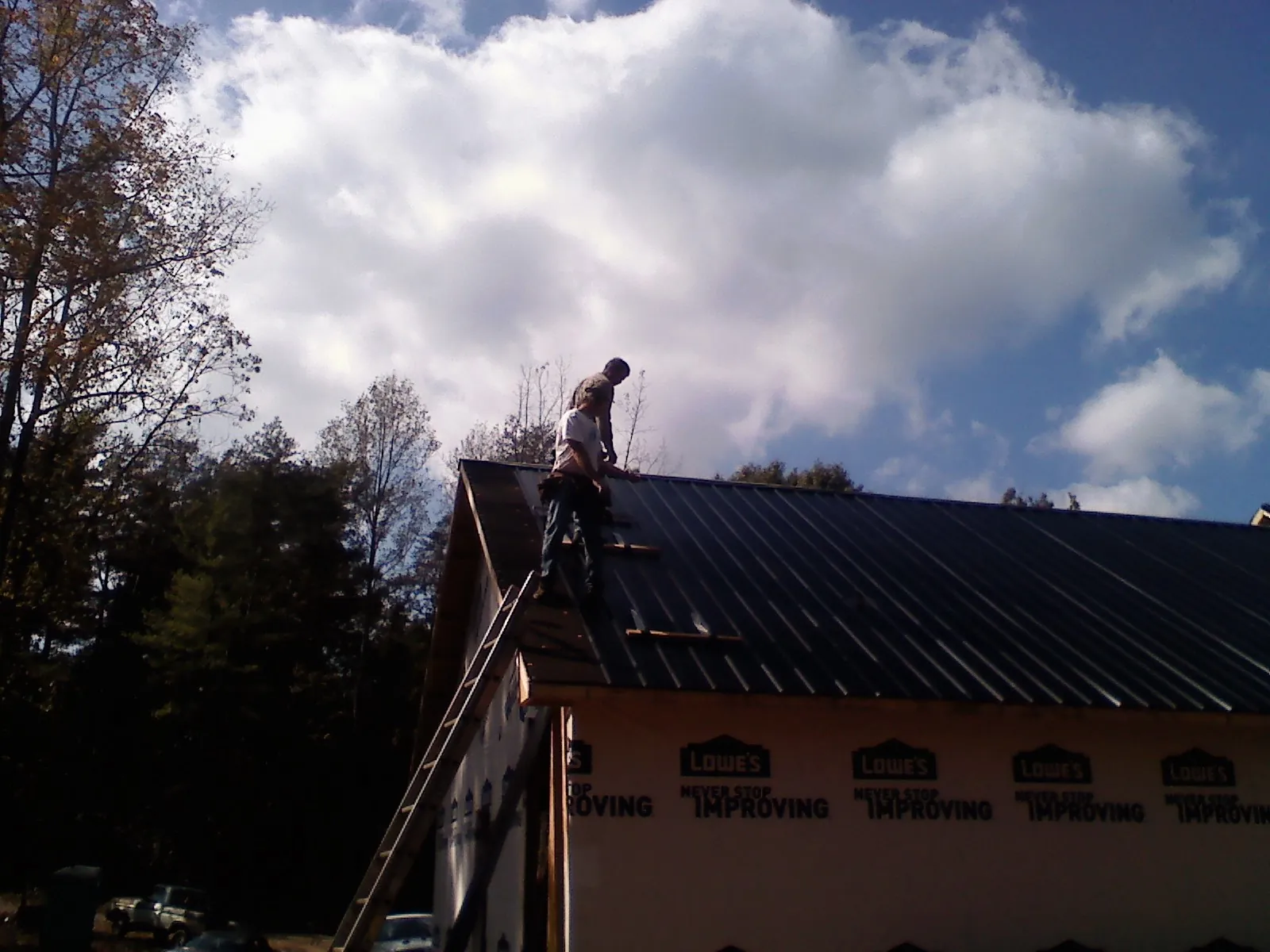Roofer fastening dark metal panels high against a cloudy sky, from a Roof Inspection job in Clarksville