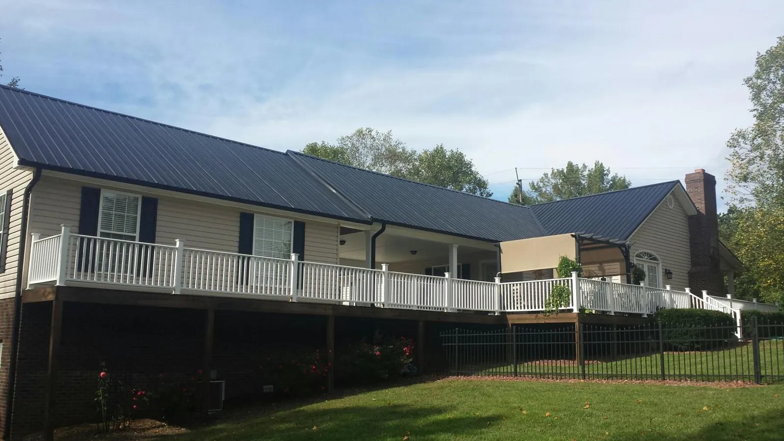 Black metal roof above a long white railed deck on a hillside home in Clarksville
